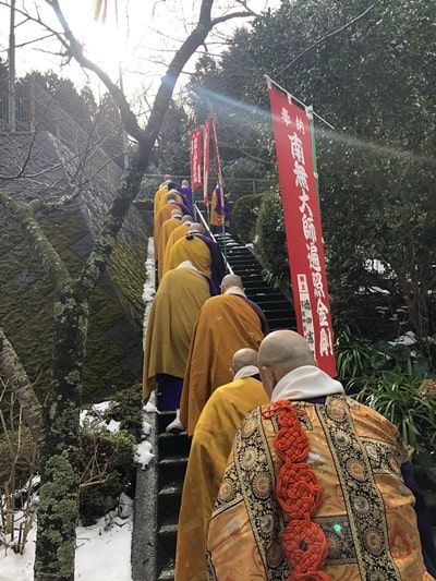 お寺の本堂に向かって並んで石段を登る僧侶たち