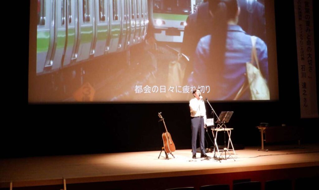 講演会の壇上で歌う石川